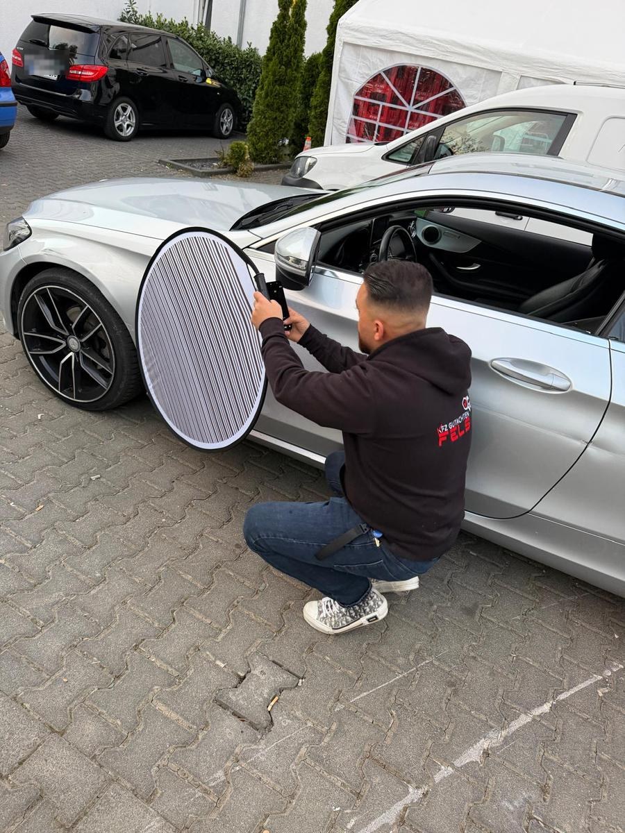 Kfz-Sachverständiger begutachtet mit dem Reflektor die Seite eines silbernen Fahrzeugs