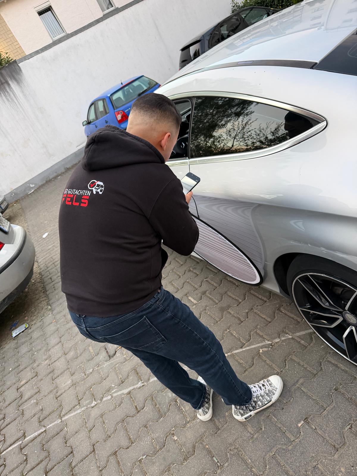 FELZ-Sachverständiger prüft mit dem Lichtreflektor die Karosserie eines silbernen Mercedes auf Unfallschäden