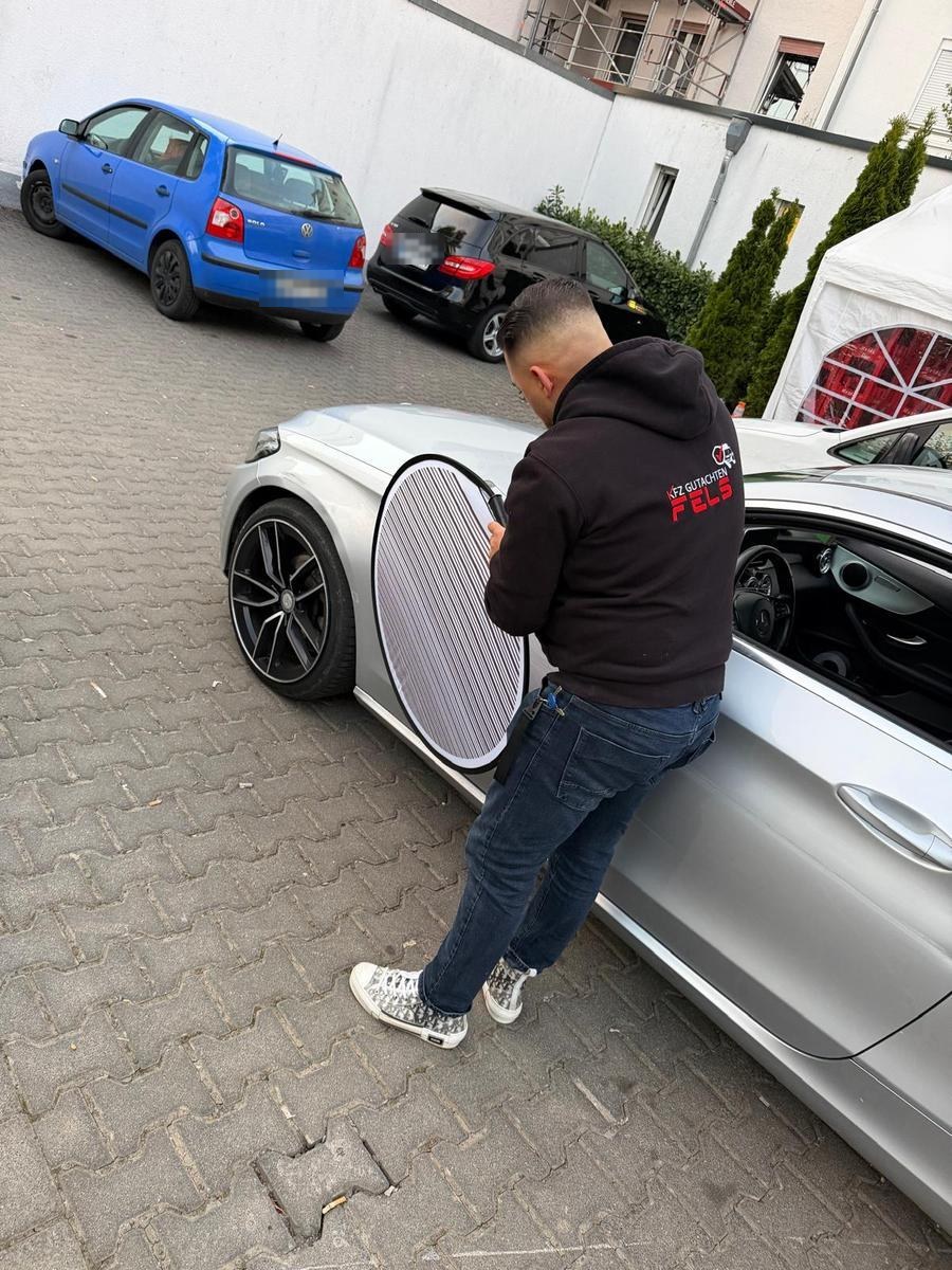 Kfz-Sachverständiger dokumentiert mit dem Reflektor Karosserieschäden an einem silbernen Fahrzeug